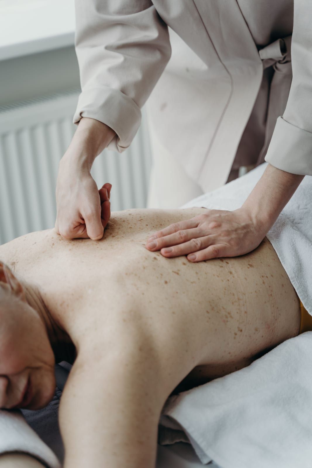 Hands pressing into a guest’s back on a massage table by a window