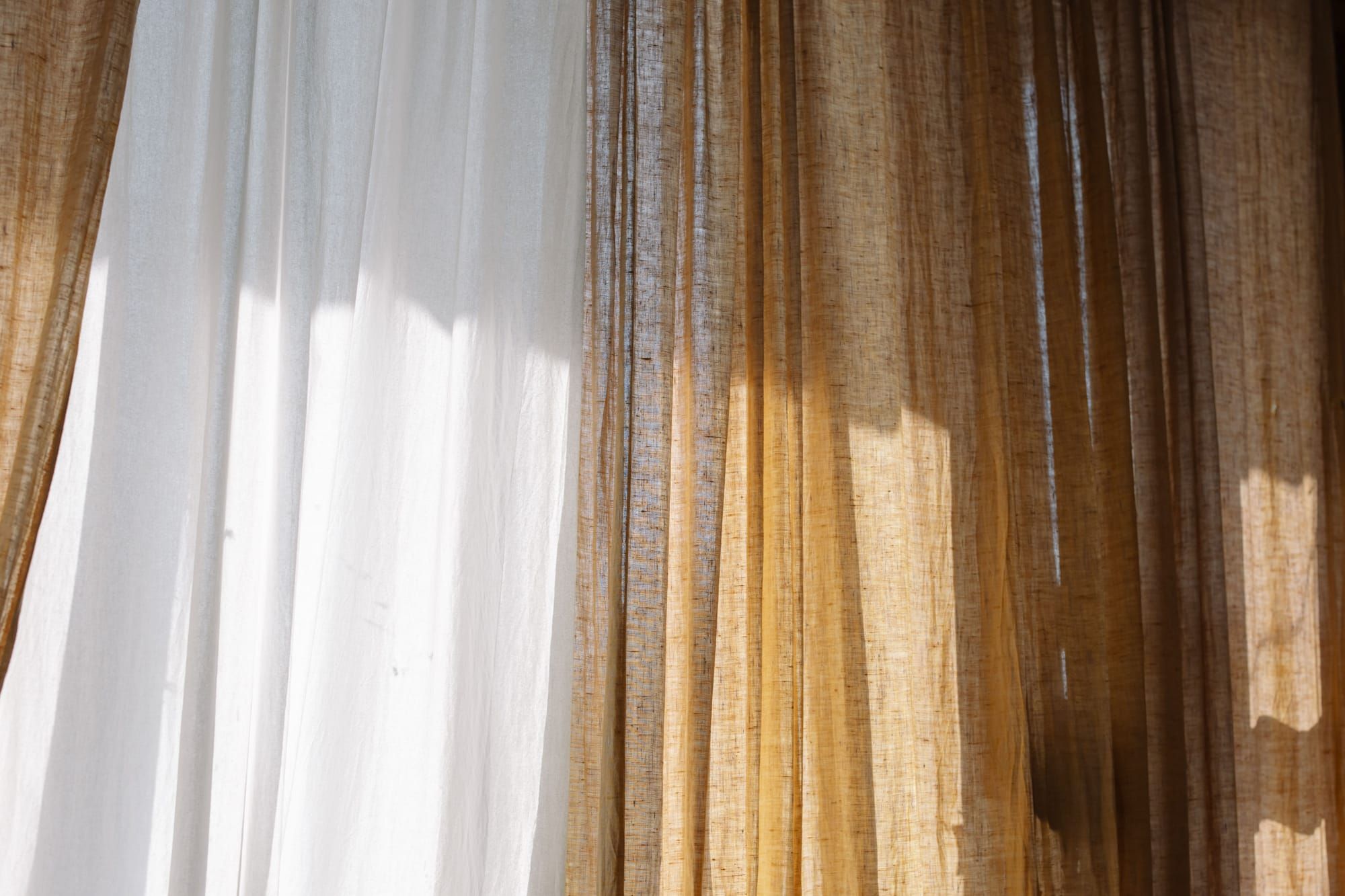Sunlight through sheer white and flax-colored linen curtains