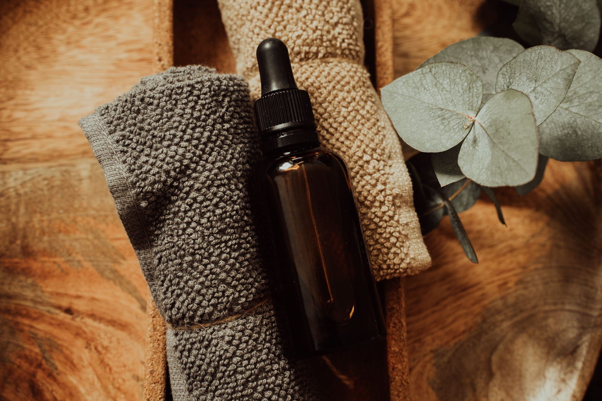 An amber dropper bottle on folded gray and oatmeal waffle towels, beside eucalyptus leaves